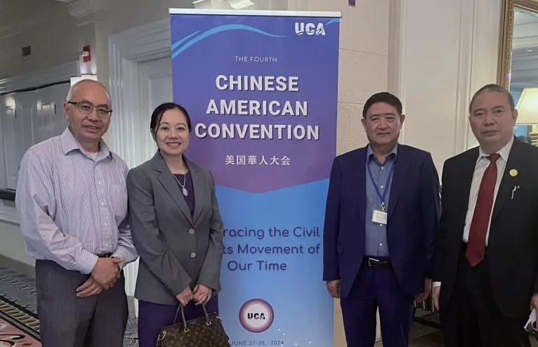 钟富华与三位其他出席者站在美国华人大会的海报前合影，背景为“Chinese American Convention”标志。