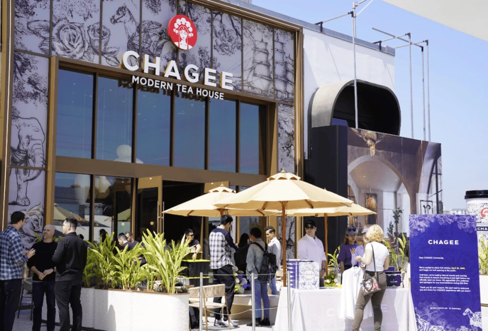 Chagee Modern Tea House 洛杉矶门店外景，门口排队的顾客和黄伞下的接待台，右侧可见品牌宣传立牌。