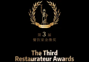A black-background poster with a golden laurel wreath encircling a stylized Statue of Liberty holding a torch. Text includes "The Restaurateur" on a ribbon, Chinese characters "第3届 餐饮家金像奖" (3rd Restaurant Industry Golden Awards), and "The Third Restaurateur Awards Nomination" in gradient gold fonts. Symmetrical design conveys prestige for Chinese culinary excellence.