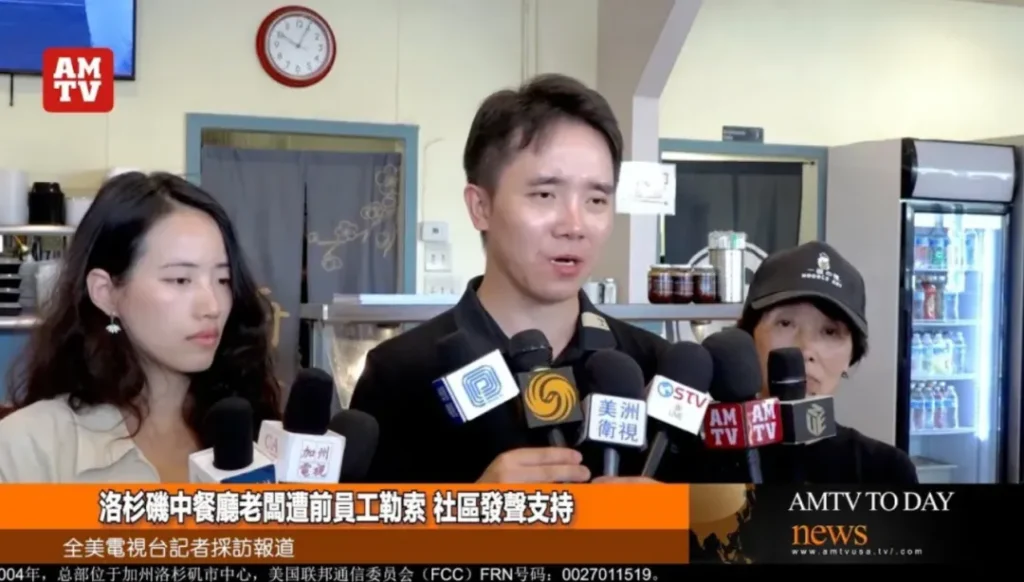 洛杉矶中餐馆老板Steven接受全美电视台专访：画面左侧老板神情凝重手持话筒，背景可见餐厅厨房冰箱与调味架；屏幕下方文字为"洛杉磯中餐廳老闆遭前員工勒索 社區發聲支持"，右上角台标AMTV标明媒体权威性，揭示餐饮业非法用工索赔风险。