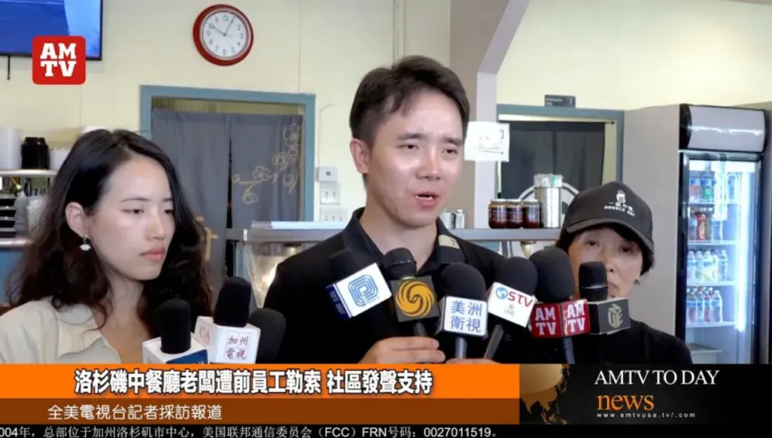 洛杉矶中餐馆老板Steven接受全美电视台专访：画面左侧老板神情凝重手持话筒，背景可见餐厅厨房冰箱与调味架；屏幕下方文字为"洛杉磯中餐廳老闆遭前員工勒索 社區發聲支持"，右上角台标AMTV标明媒体权威性，揭示餐饮业非法用工索赔风险。