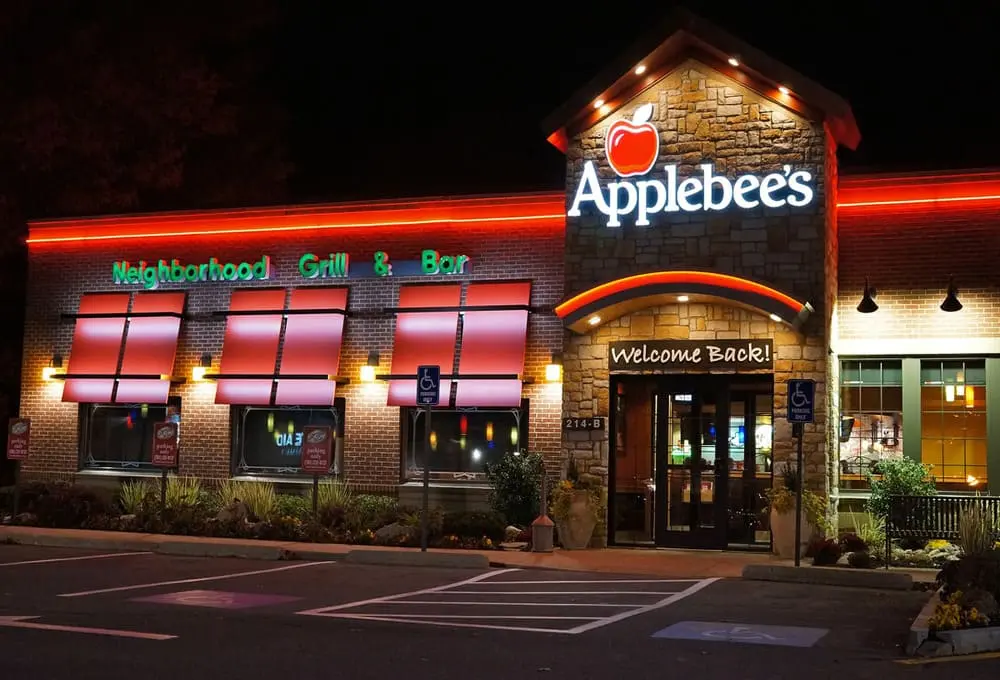 Applebee's餐厅砖砌外墙配红色霓虹灯招牌，"Neighborhood Grill & Bar"字样与绿植门廊营造美式休闲氛围。呼应正文"中档餐厅客流量下滑4.2%"现状。
