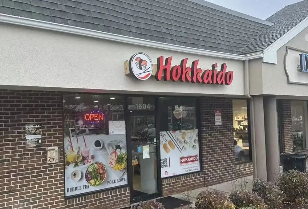 "Hokkaido Cafe餐厅外景：砖墙灰瓦建筑，醒目红色招牌下，玻璃窗展示着POKE BOWL和BUBBLE TEA宣传图。入口上方亮绿色OPEN灯箱，门侧有餐牌架，突显日式快餐与奶茶结合的特色。"