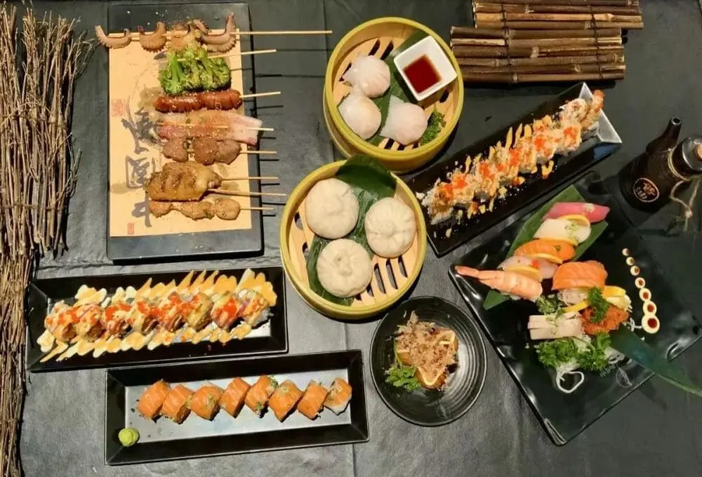 "Samurai Buffalo人气菜品拼盘：炭烤鸡肉串配彩椒、蒸饺蘸辣酱、三文鱼寿司卷，搭配鲑鱼刺身与玉子烧。竹制餐具衬托新鲜食材，展现传统日料与美式烧烤的创新融合。"