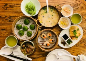餐桌陈列蒸笼（蔬菜包、酥饺）、粥锅及小份鸡块配汤，证明中式聚餐可通过份量控制与蒸煮实现轻负担。