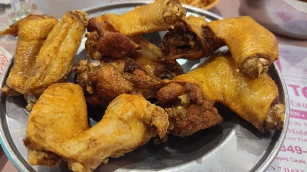 金属盘盛放金黄炸鸡翅，表皮酥脆微焦，堆叠如小山，配酸梅酱蘸碟。背景虚化可见餐厅环境，呈现40年广东家传技法精髓。