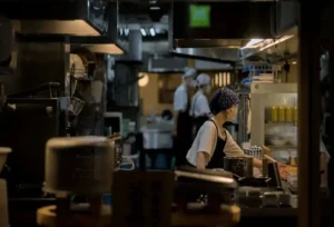 专业厨师团队有序协作，主厨专注处理食材，背景人员配合操作设备。展示标准化厨房运作与团队稳定性。