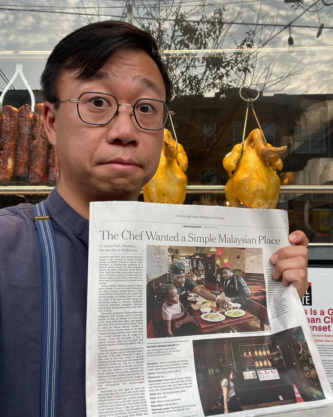 导演Christopher Low（戴眼镜穿深蓝衬衫）在海南鸡记店前手持《纽约时报》报道，头条标题"The Chef Wanted a Simple Malaysian Place"清晰可见。背景橱窗悬挂油亮烤鸡，报道副标题"Sunset Park, Brooklyn, the specialty is chicken rice"印证文中"50平米小店登纽约时报百佳榜"逆袭叙事，婚戒细节暗示家族传承使命。