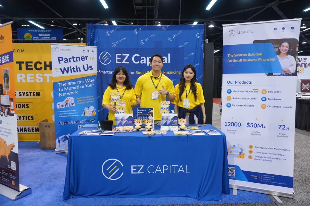 三位黄衫顾问驻守EZ Capital展位，背景横幅宣导"小企业智慧融资"。桌面试算表模板展示贷款推演流程，www.toeexpo.com官网标牌引导线上服务。左侧竞品黄板反衬蓝黄主调专业度，灯箱强调"2025 TASTE OF ASIA"时效属性。