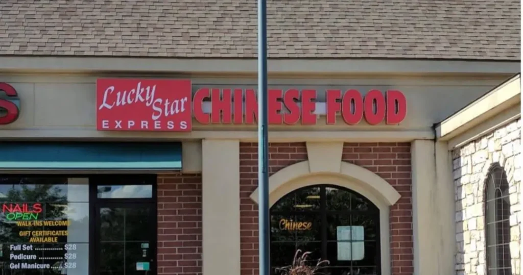 图片展示“Lucky Star Express”中式快餐店招牌（红底白字），右侧配“CHINESE FOOD”立体字；相邻美甲店橱窗贴有“NAILS”“OPEN”灯箱及美甲价目表（全套$28），门框为拱形玻璃设计，背景可见电线杆与红砖外墙。