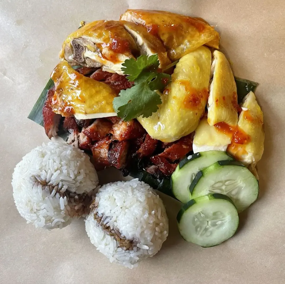 Low家族秘制双拼：左为骨肉分离海南鸡配三味碟（黑酱油醇厚/姜葱酱辛香/辣椒酱刺激），右置蜜汁五花腩叉烧（焦糖脆皮+琥珀色油脂层）。底部油纸包裹鸡油饭团，青瓜片解腻，还原文中"拆礼物式怀旧仪式感"。