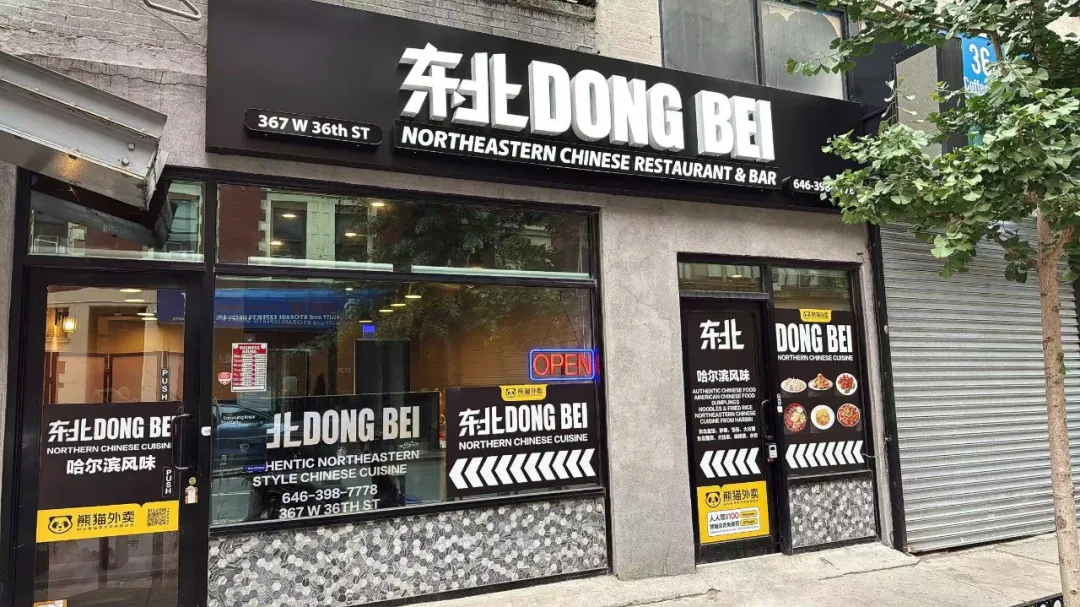 367 W 36th ST街边，“东北 DONG BEI”黑底白字招牌，标“哈尔滨风味”，橱窗贴“OPEN”，外墙贴瓷砖，侧有树。