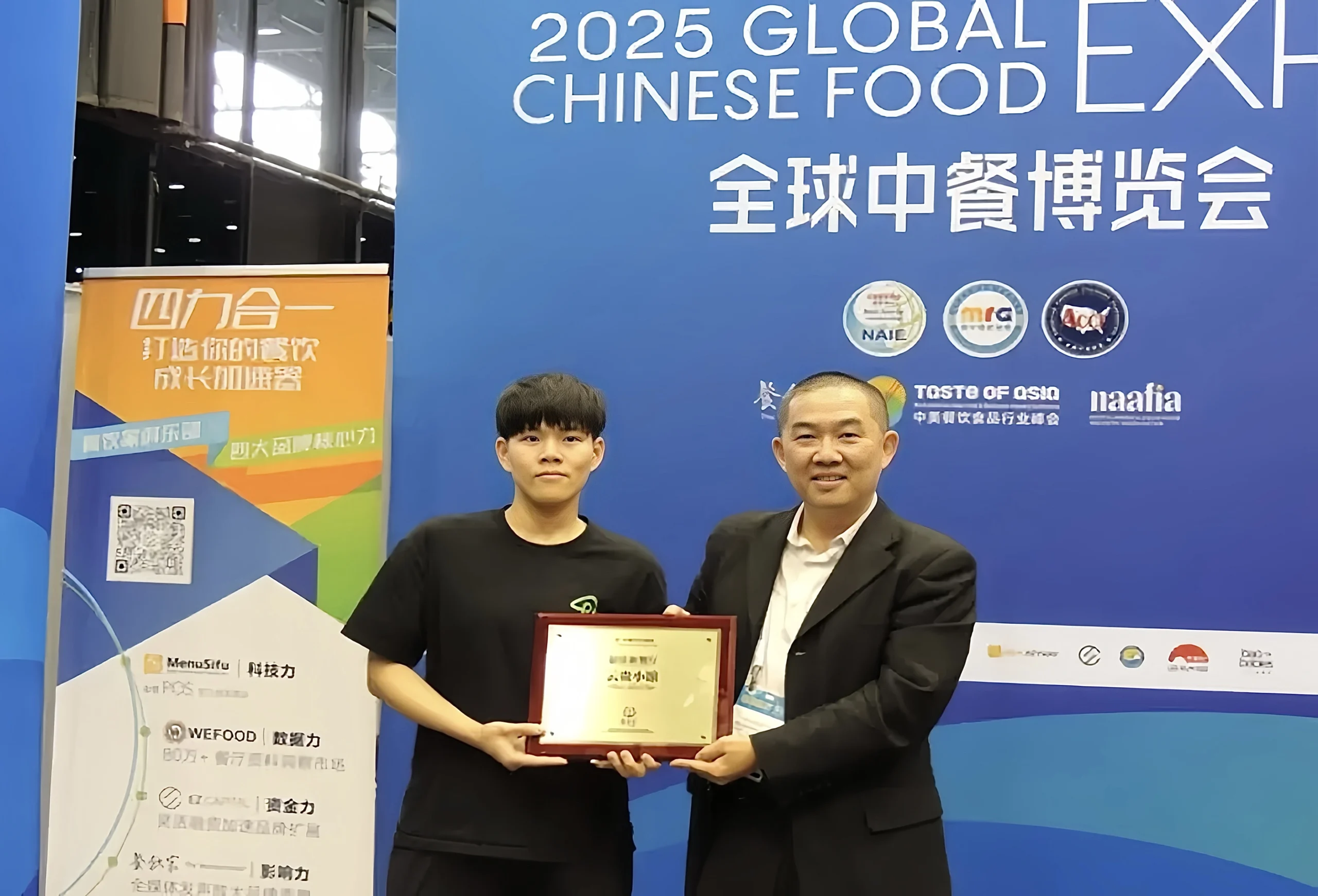 在2025全球中餐博览会现场，熊猫教授李志杰（右）为云贵小馆代表颁发奖牌。两人共同手持奖牌，在展会背景板前合影留念。