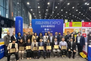 在2025全球中餐博览会现场，参展嘉宾与获奖者合影。前排坐着的获奖代表手持奖牌，背景是印有‘2025 Global Chinese Food Expo’标识的展板与展会展位。