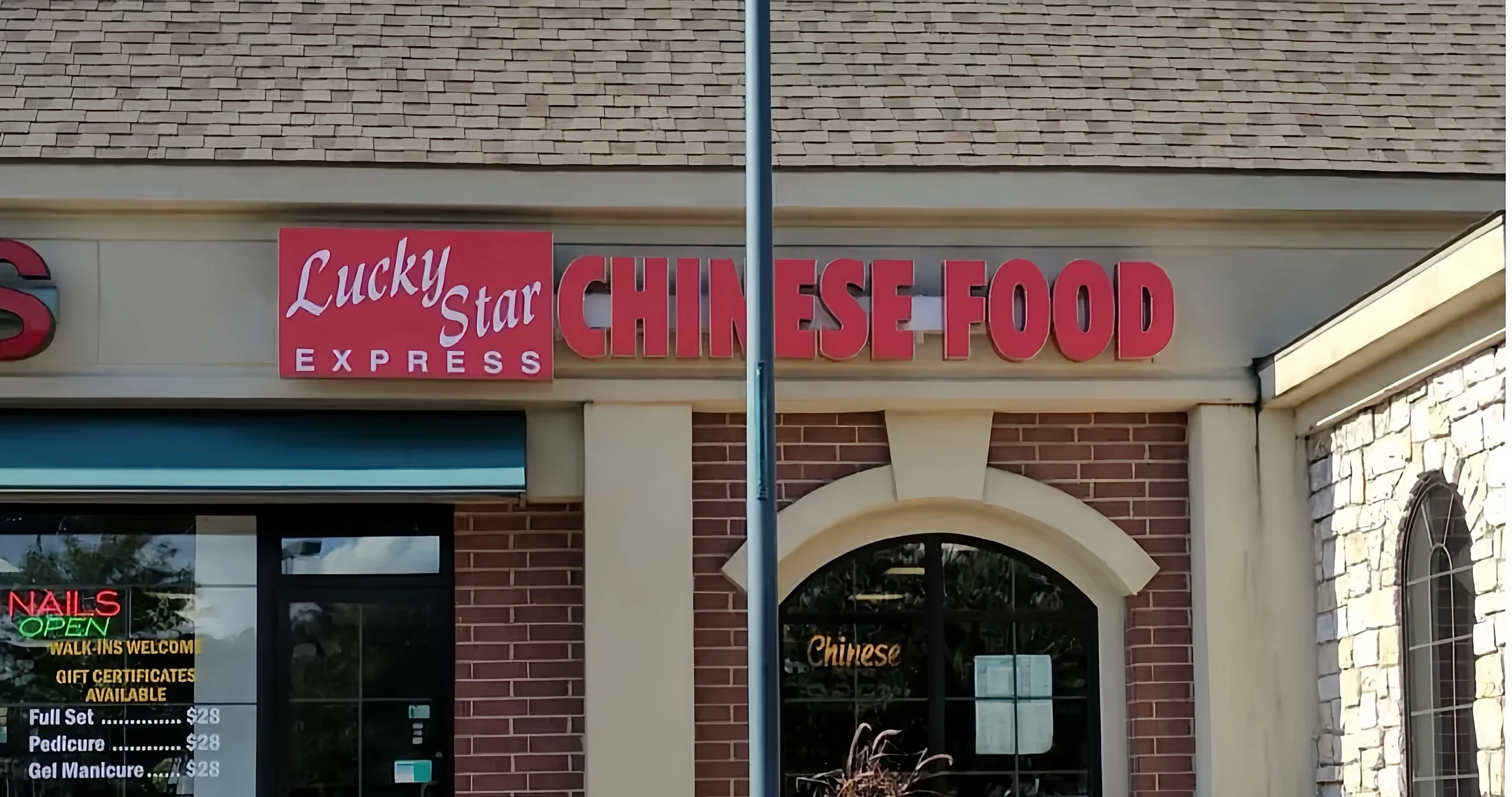 图片展示“Lucky Star Express”中式快餐店招牌（红底白字），右侧配“CHINESE FOOD”立体字；相邻美甲店橱窗贴有“NAILS”“OPEN”灯箱及美甲价目表（全套$28），门框为拱形玻璃设计，背景可见电线杆与红砖外墙。