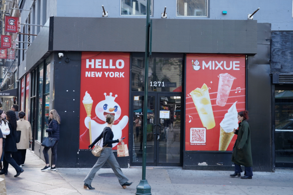 蜜雪冰城纽约1271号门店，红底广告牌含“HELLO NEW YORK”、饮品图案、二维码，门前行人，背景是城市街道。