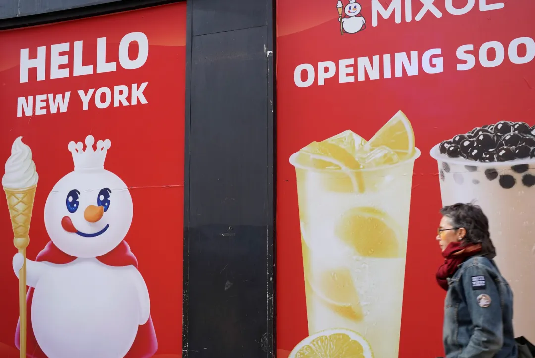 红色背景蜜雪冰城开业海报，左侧雪人举冰淇淋配“HELLO NEW YORK”，右侧饮品配“OPENING SOON”，一女士从旁走过。