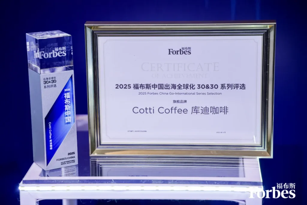 玻璃台置奖杯证书，有“福布斯”“2025出海全球化30&30”字样，标注库迪咖啡获年度品牌奖，背景蓝色。